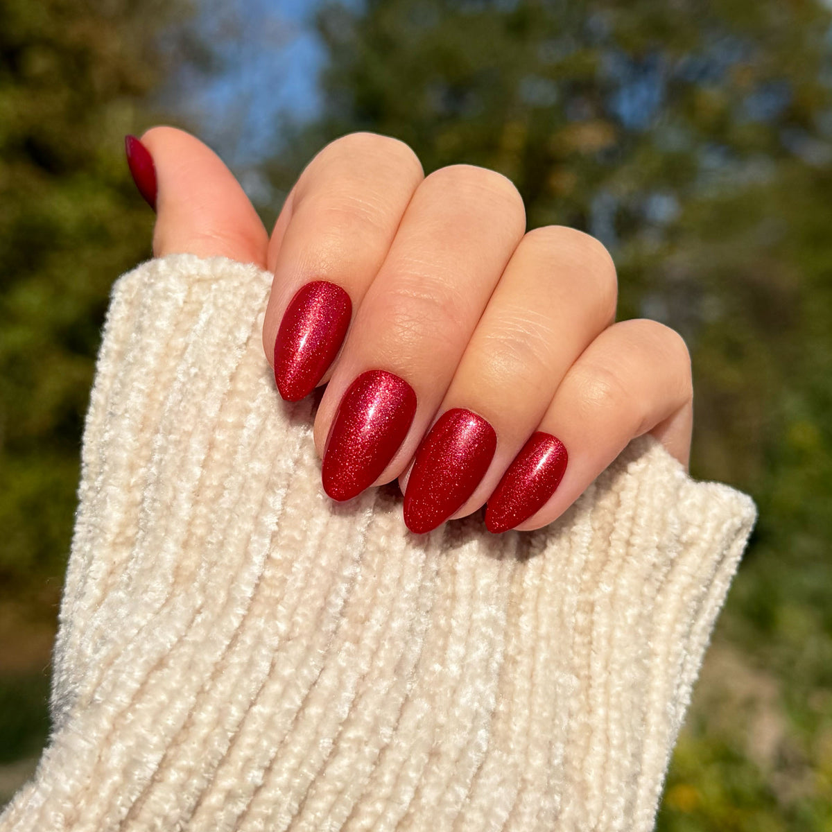Angewinkelte Hand mit Soft Gel Press-On Nails „Spiced Cherry“ in Kirschrot mit Schimmer, kurz und mandelförmig.