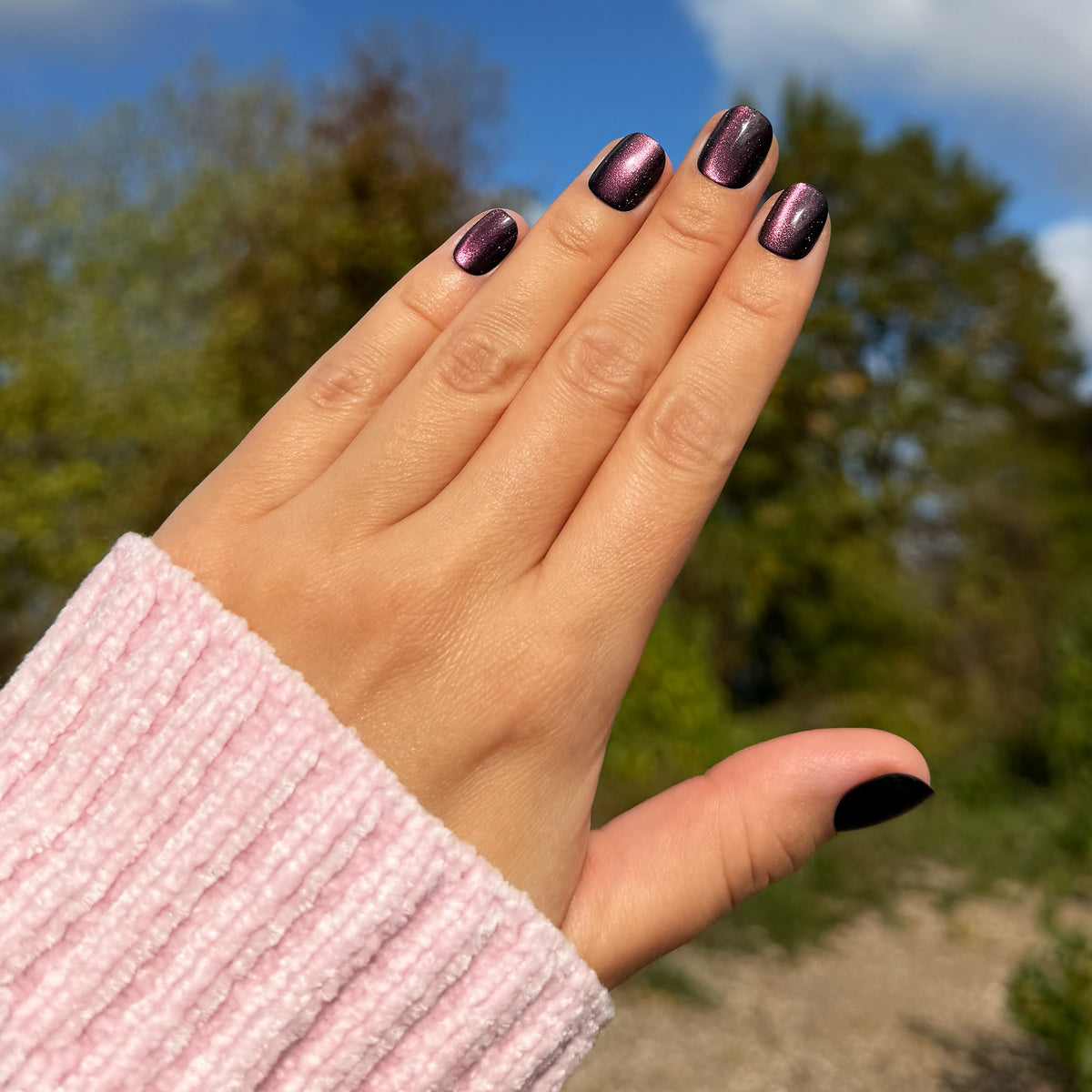 Hand mit Soft Gel Press-On Nails „Plum Glow“ in dunklem Pflaumenton mit Schimmer, kurz und rund.