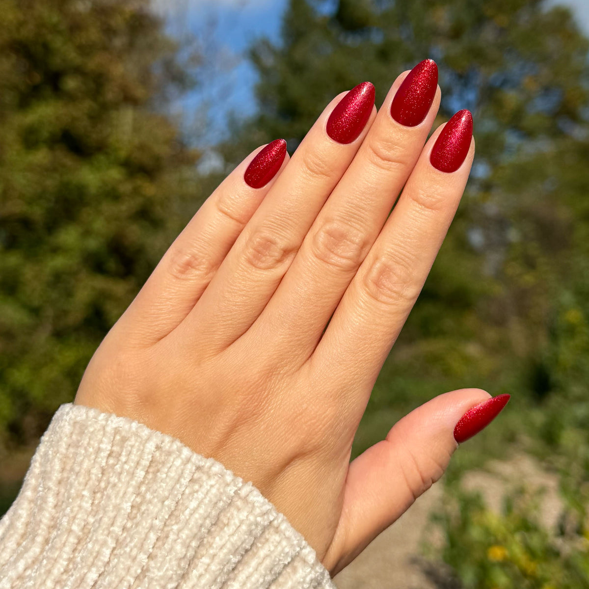 Hand mit Soft Gel Press-On Nails „Spiced Cherry“ in Kirschrot mit Schimmer, kurz und mandelförmig.